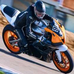Rider in black Alpinestars leathers on an orange and black motorcycle; leaning into a turn, seen from a front three-quarter angle