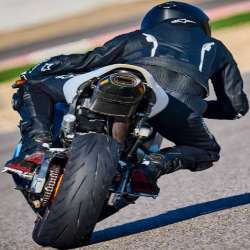 Rider in black Alpinestars leathers on an orange and black motorcycle; photographed from behind, with the back of the rider and motorcycle visible and no race number in view
