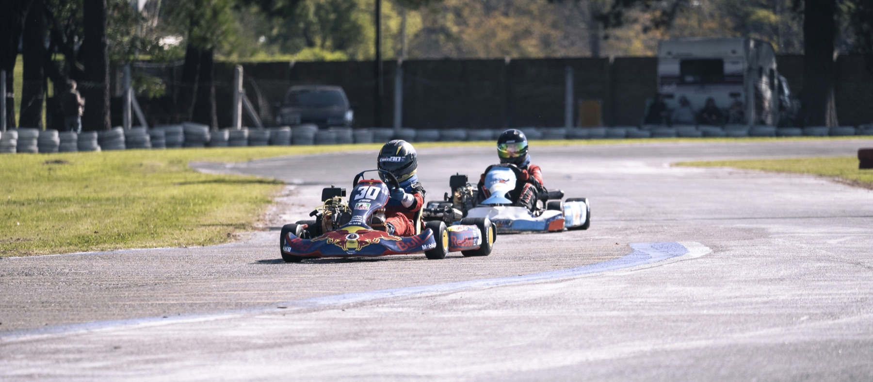 Two helmeted kart racers following a bend on an outdoor circuit.