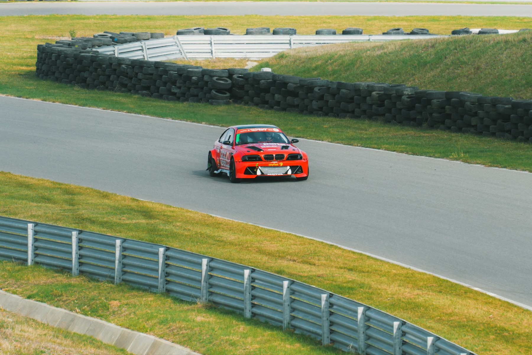 Red race car on a circuit beside tyre barriers.