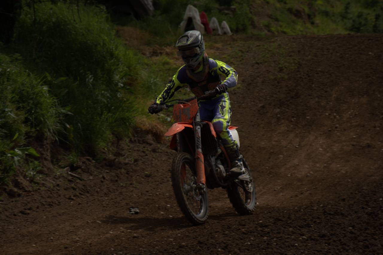 A rider on an orange dirt bike with mud obscuring the front number plate.
