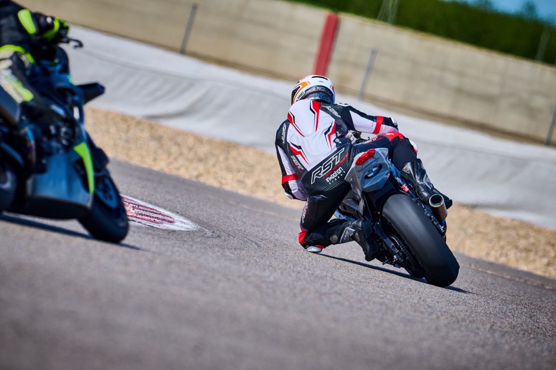 Motorcycle riders leaning through a circuit corner, photographed from behind with no readable race numbers